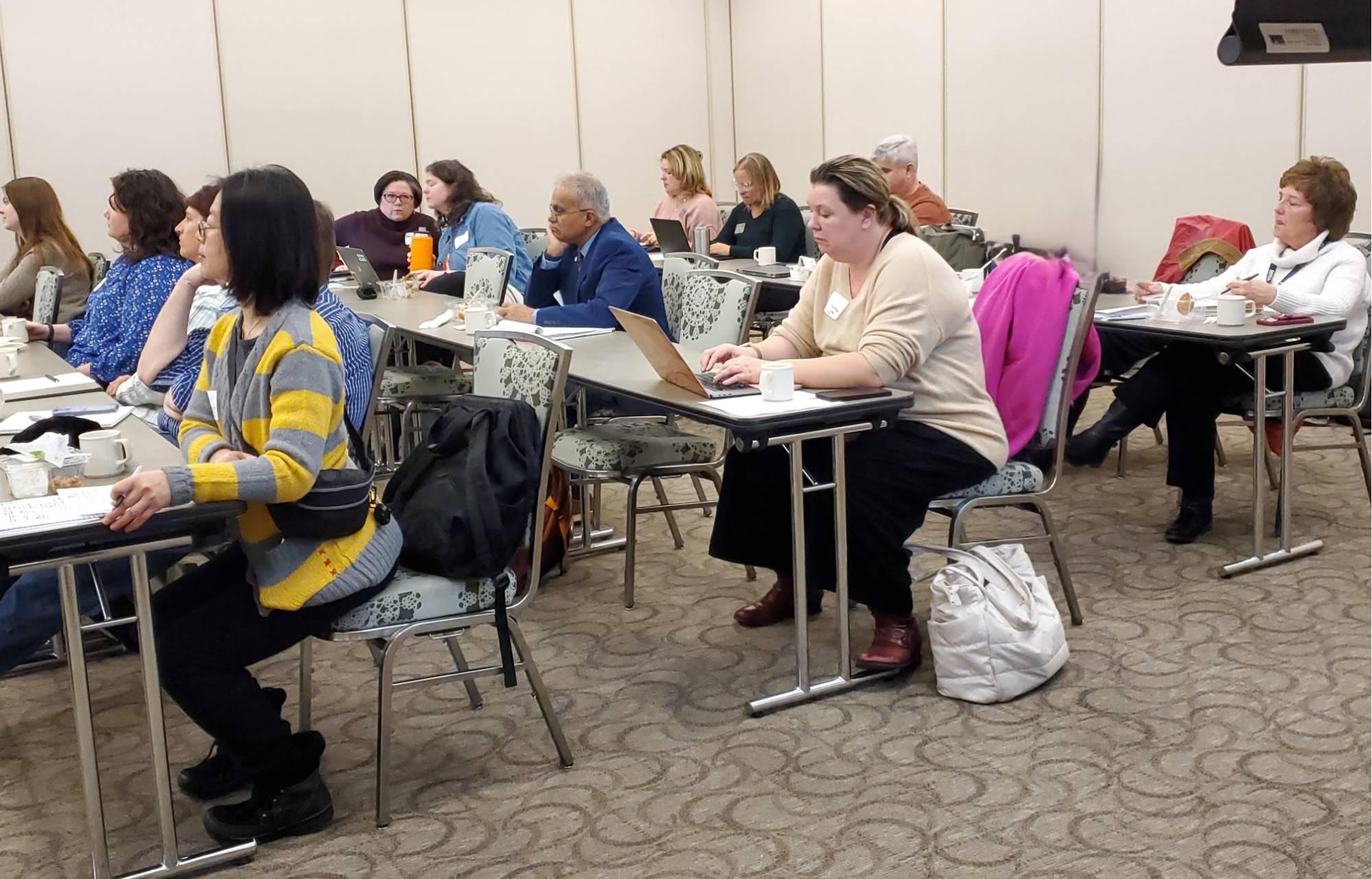 Conference attendees listening to and taking notes on a presentation